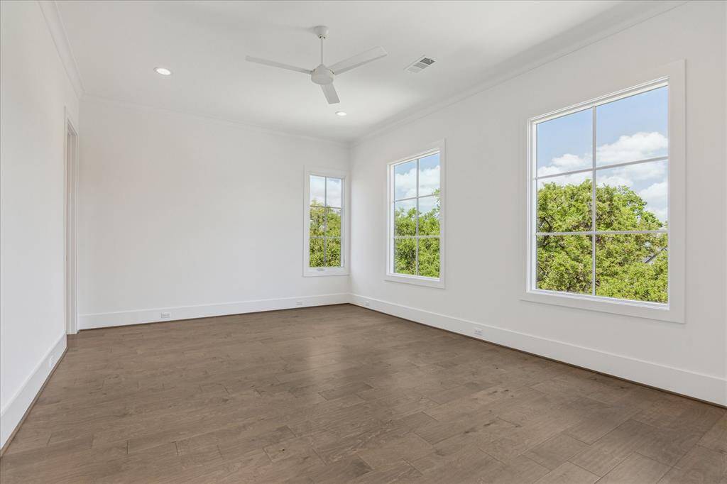 This spacious secondary bedroom is filled with natural light from large windows and features wood flooring, high ceilings, and a neutral palette, creating a bright and versatile space.