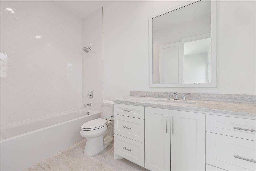 This en suite bath features a spacious vanity with ample storage, a large framed mirror, and a tub-shower combination with elegant herringbone tile surround, offering a clean and polished look.