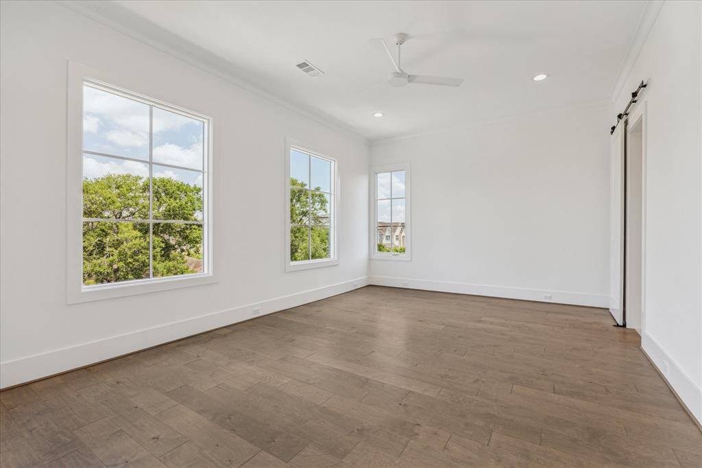 This generously sized secondary bedroom offers an abundance of natural light from multiple large windows, complemented by high ceilings, wood flooring, and a clean, open layout ideal for various uses.