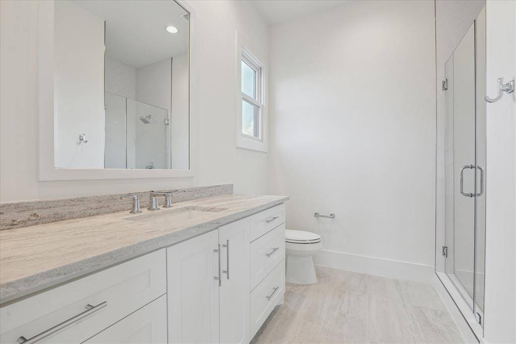 This secondary en suite bath features a spacious vanity with ample storage, a walk-in shower with frameless glass enclosure, and a bright, airy feel complemented by a window bringing in natural light.