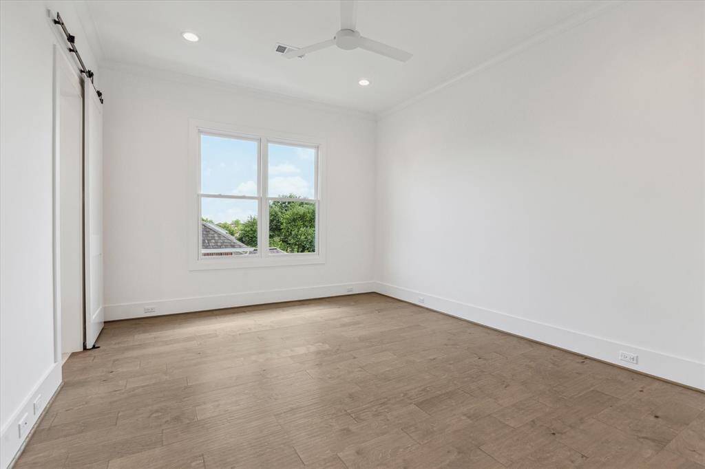 This secondary bedroom offers a spacious layout with high ceilings, large windows that provide abundant natural light, and a walk-in closet with sliding barn-style doors for added functionality.