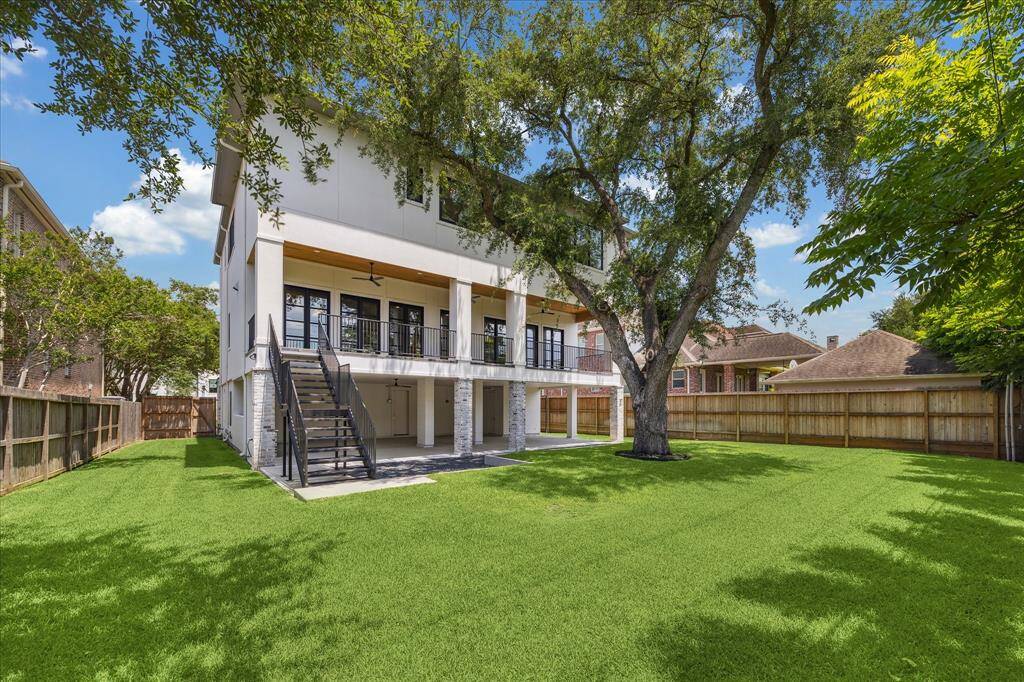 This spacious backyard offers a generous expanse of green lawn shaded by mature trees, providing plenty of room for play, entertaining, or future outdoor projects. The covered patio and elevated balcony create multiple levels of outdoor living, seamlessly connecting the indoors to the open yard below.