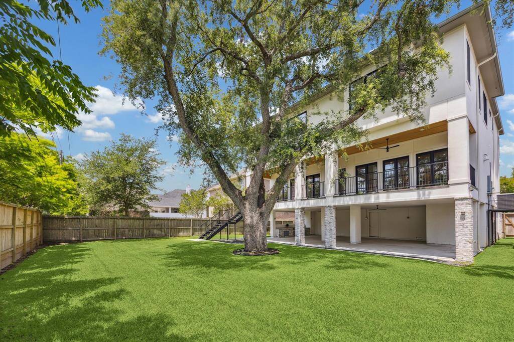 This backyard offers a wide, open lawn framed by privacy fencing and mature trees, creating a peaceful, shaded retreat. The elevated terrace overlooks the green space, while the expansive covered patio below adds versatility for outdoor gatherings, play, or relaxation.