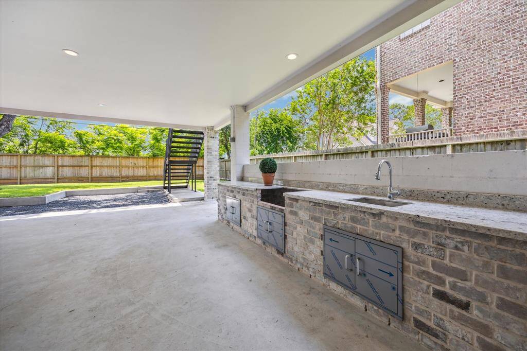 This covered outdoor kitchen is designed for all-weather entertaining, featuring a space for a grill station, sink, and prep counters set in durable stonework. Overlooking the backyard, it offers a seamless connection to the surrounding green space while providing shade and comfort for outdoor cooking and gatherings.