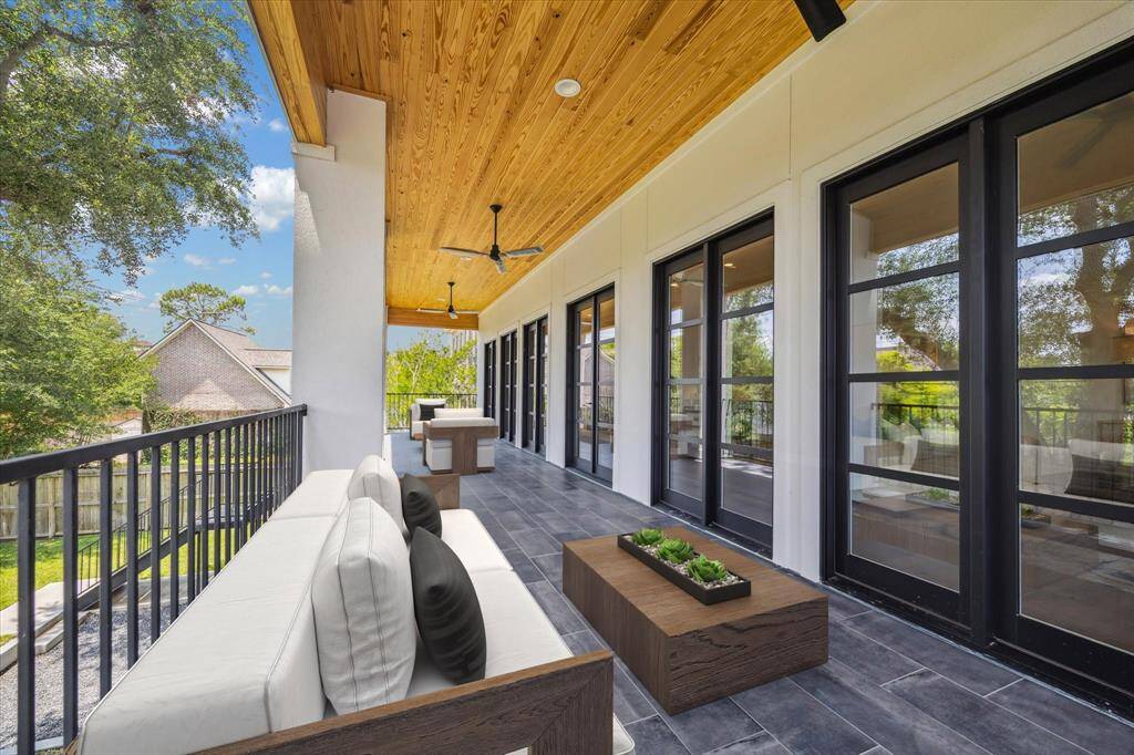 This expansive outdoor patio stretches along the back of the home, offering an elevated view of the backyard. The space is finished with a wood-paneled ceiling, ceiling fans, and sleek tile flooring, all designed to create a comfortable and stylish setting for open-air relaxation and entertaining. Multiple glass doors connect seamlessly to the interior, enhancing the indoor-outdoor flow. *virtually staged