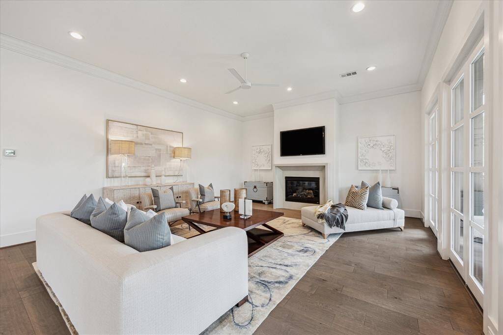 This spacious living room features a corner fireplace, expansive windows, and French doors that fill the space with natural light and offer seamless indoor-outdoor connectivity.