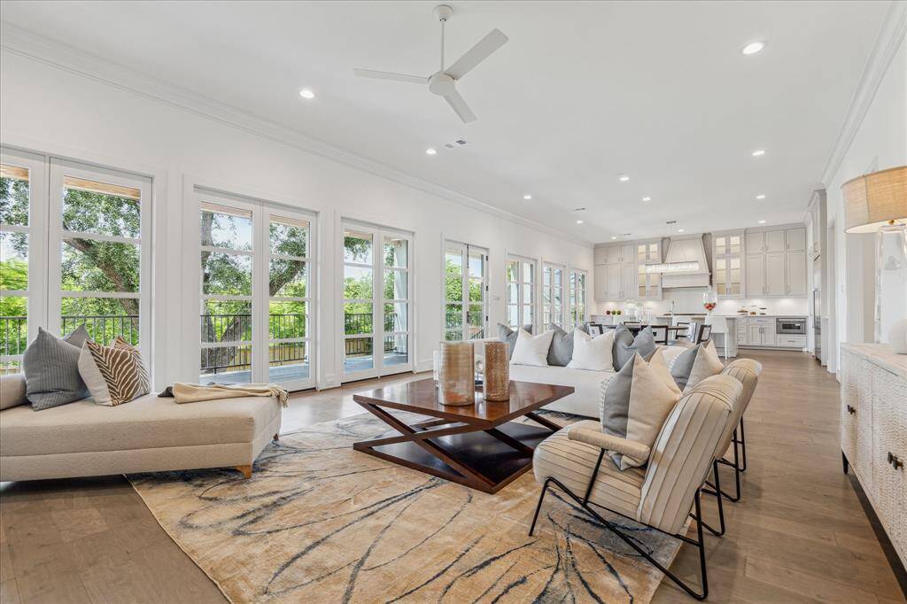 This light-filled living room seamlessly connects to the kitchen and dining areas, with walls of windows and French doors enhancing the open-concept design and providing effortless indoor-outdoor flow.