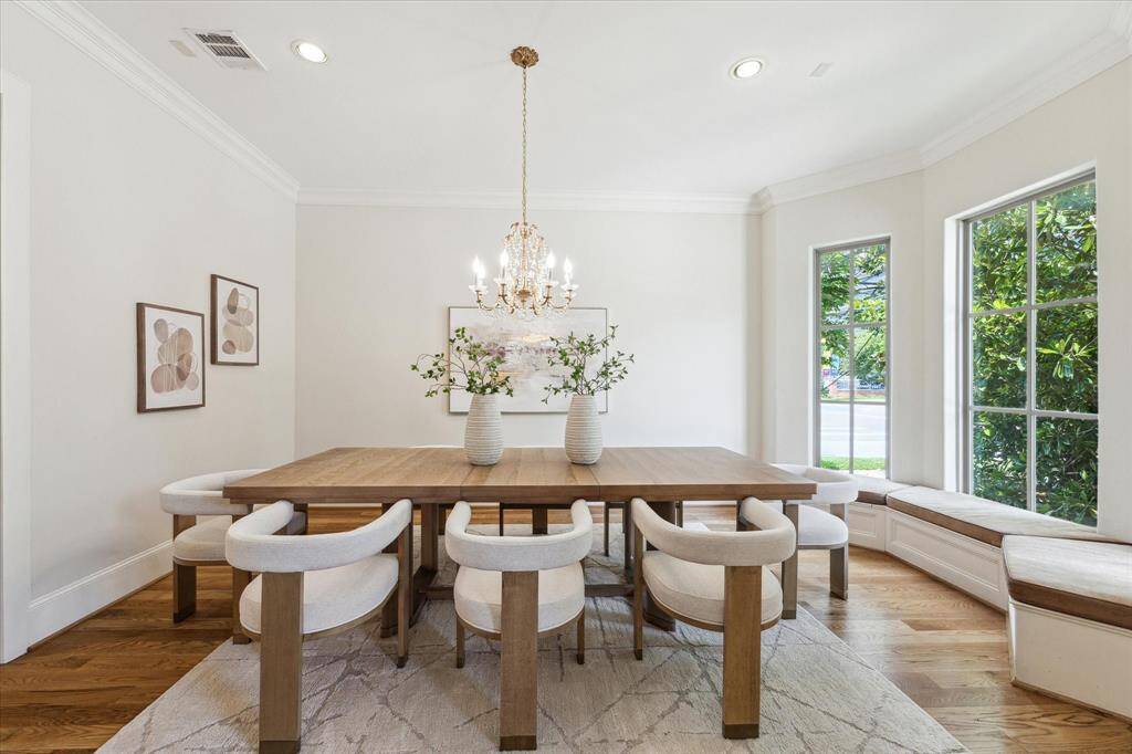 The dining room features bay windows with a custom bench, hardwood floors, and recessed lighting, all anchored by a beautiful chandelier.