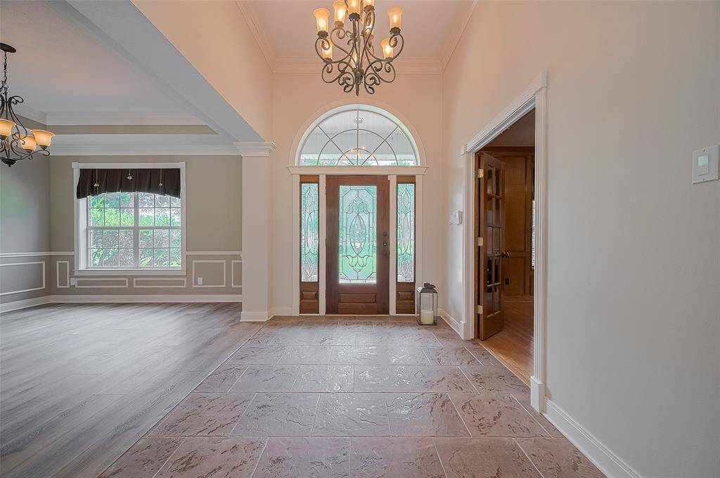 WELCOME!  Gorgeous earth-toned tile flooring in the entry extends  through the family room.   Elegant chandelier offers a touch of elegance while adding to the abundant natural light.  To the left is the dining room with recent vinyl plank flooring.  The right is the home office.