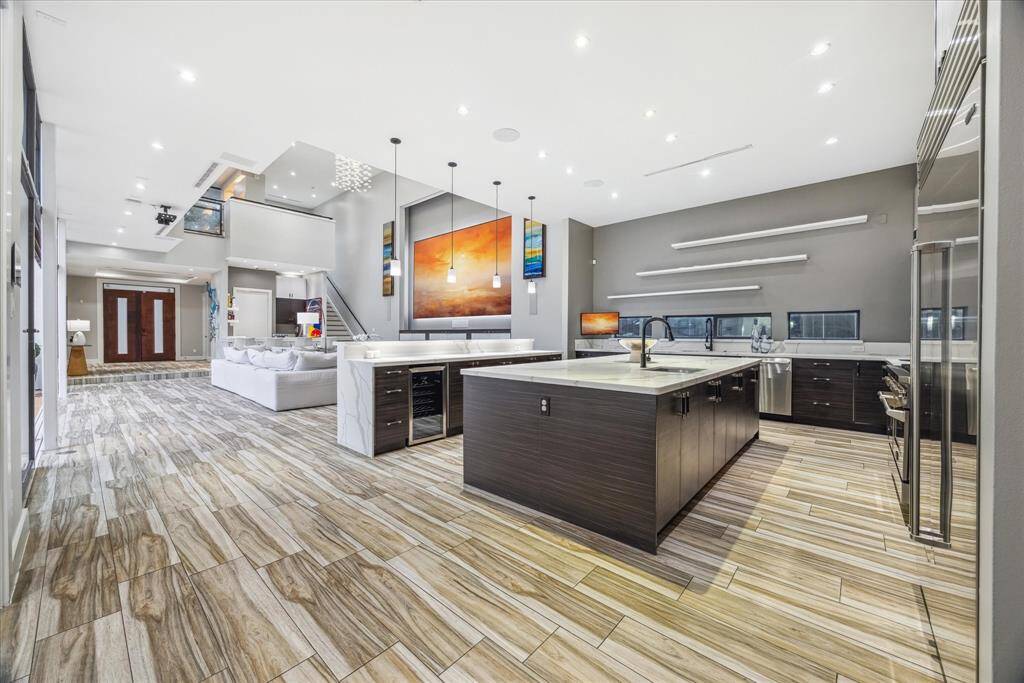 This photo showcases a spacious, modern open-concept living area with a sleek kitchen island, stylish pendant lighting, and wood-patterned flooring. The room is well-lit with recessed lighting.