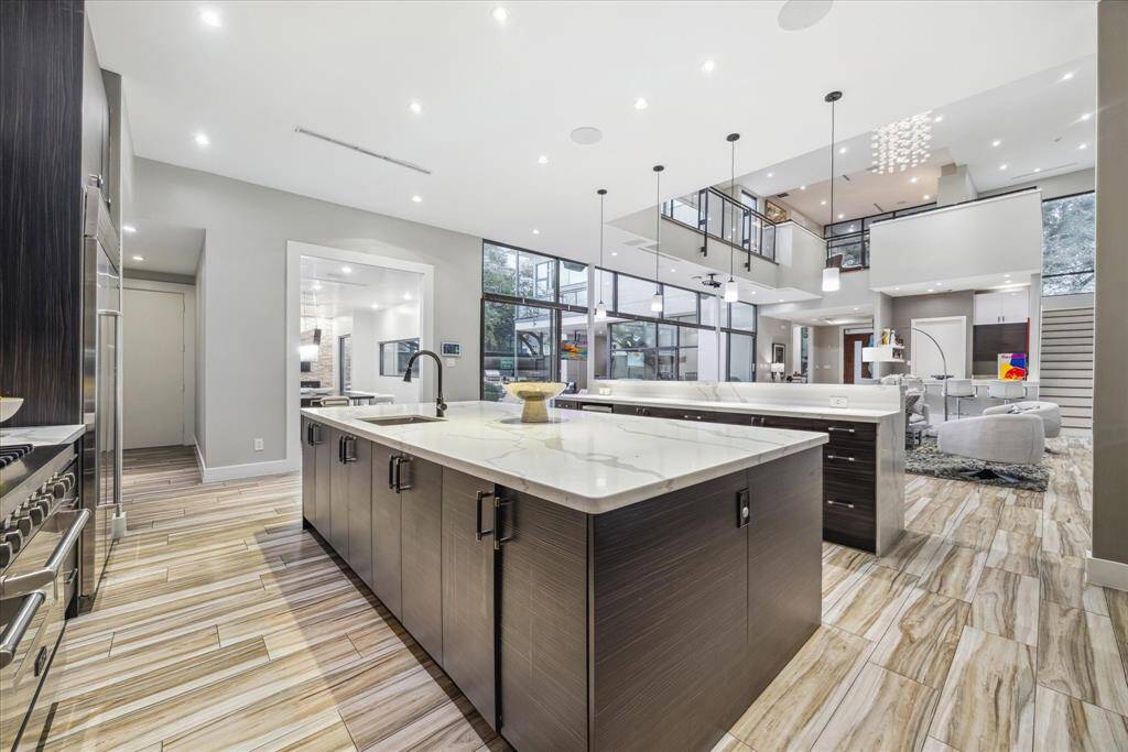 This modern home features a spacious, open-concept kitchen and living area with high ceilings and abundant natural light. The kitchen boasts sleek cabinetry, a large island with marble countertops, and premium stainless steel appliances. The elegant tile flooring seamlessly connects to a stylish living space perfect for entertaining.