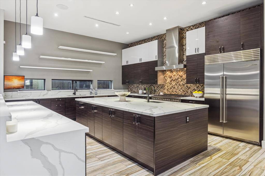 This modern kitchen features sleek dark cabinetry, a spacious island with a marble countertop, and stainless steel appliances. It has ample lighting, a stylish backsplash, and open shelving for a contemporary touch.