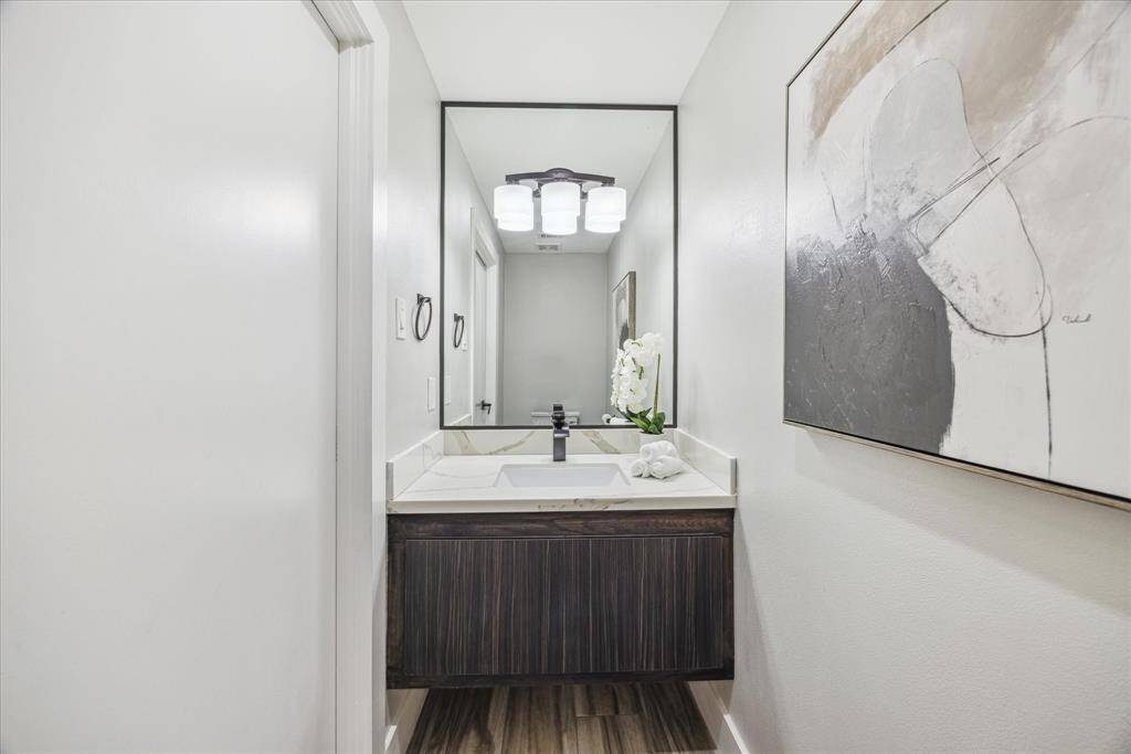 This is a modern, half bathroom featuring a sleek vanity with a white countertop and an under-mount sink. A large mirror and contemporary light fixture enhance the space.