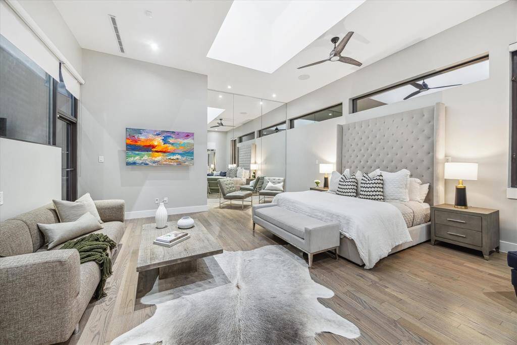 This spacious bedroom features a modern design with high ceilings, a large skylight, and hardwood floors.