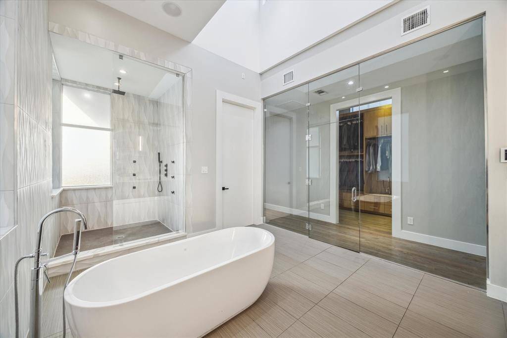 This photo showcases a modern bathroom featuring a sleek freestanding bathtub, a spacious glass-enclosed shower, and an adjacent walk-in closet with glass doors, all set in a bright, minimalist design.