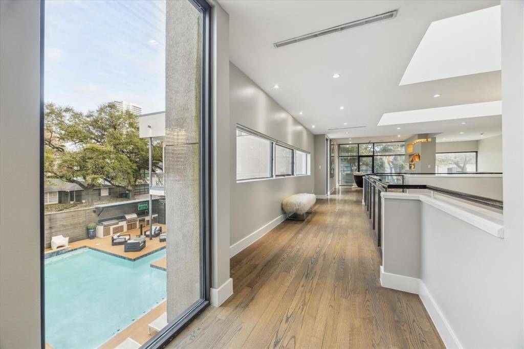 This modern home features a bright hallway with large windows overlooking a pool area. The sleek interior design includes hardwood floors and ample natural light, creating an inviting and spacious atmosphere.