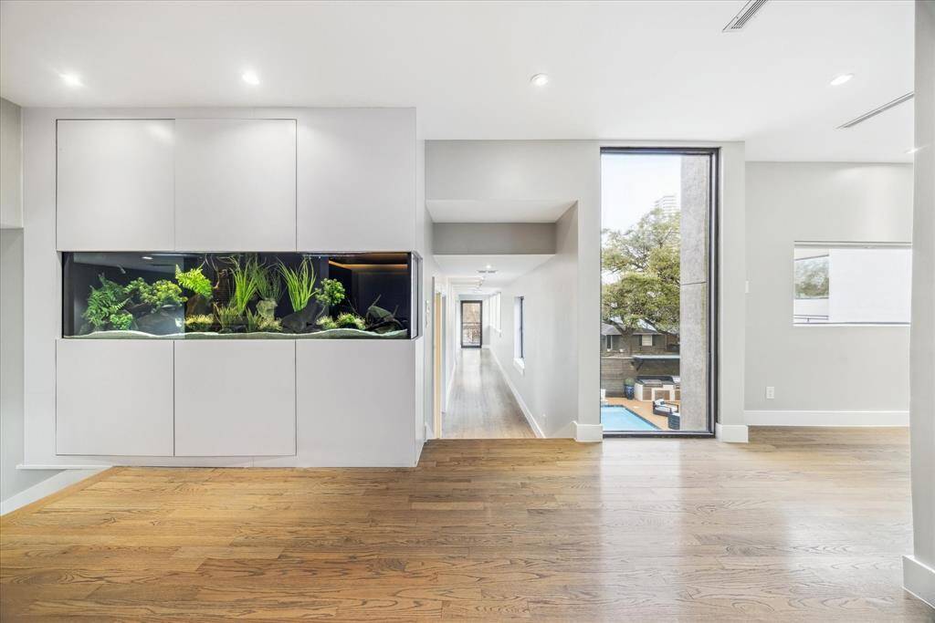 This spacious home features a modern interior with hardwood floors and a built-in aquarium. Large windows provide abundant natural light and a view of the outdoor pool area. The open hallway creates a seamless flow through the space.
