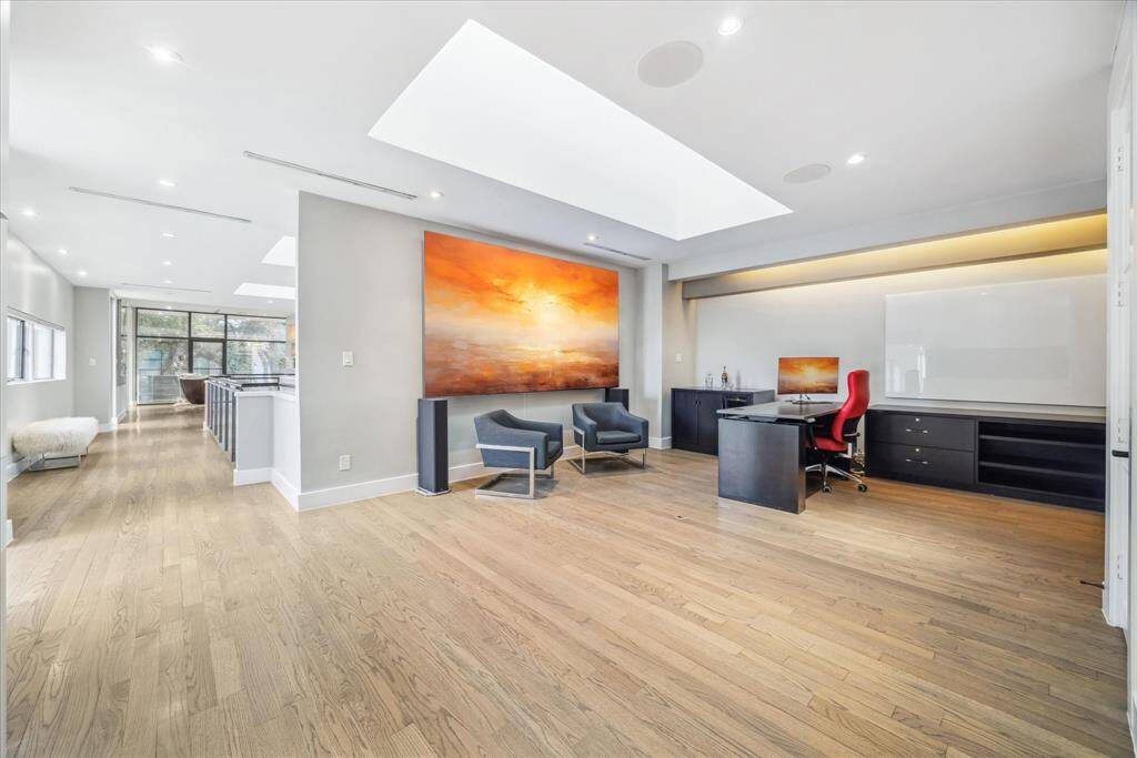 This spacious, modern room features hardwood floors, a large skylight, and ample natural light. The open layout flows into a bright area with large windows, enhancing the airy feel.