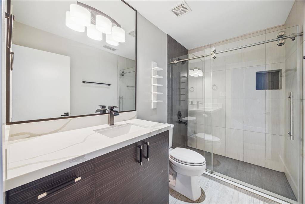 This modern bathroom features a sleek vanity with a large mirror, a vessel sink, and stylish lighting. It includes a spacious walk-in shower with a glass door and contemporary tilework, creating a clean and elegant look.