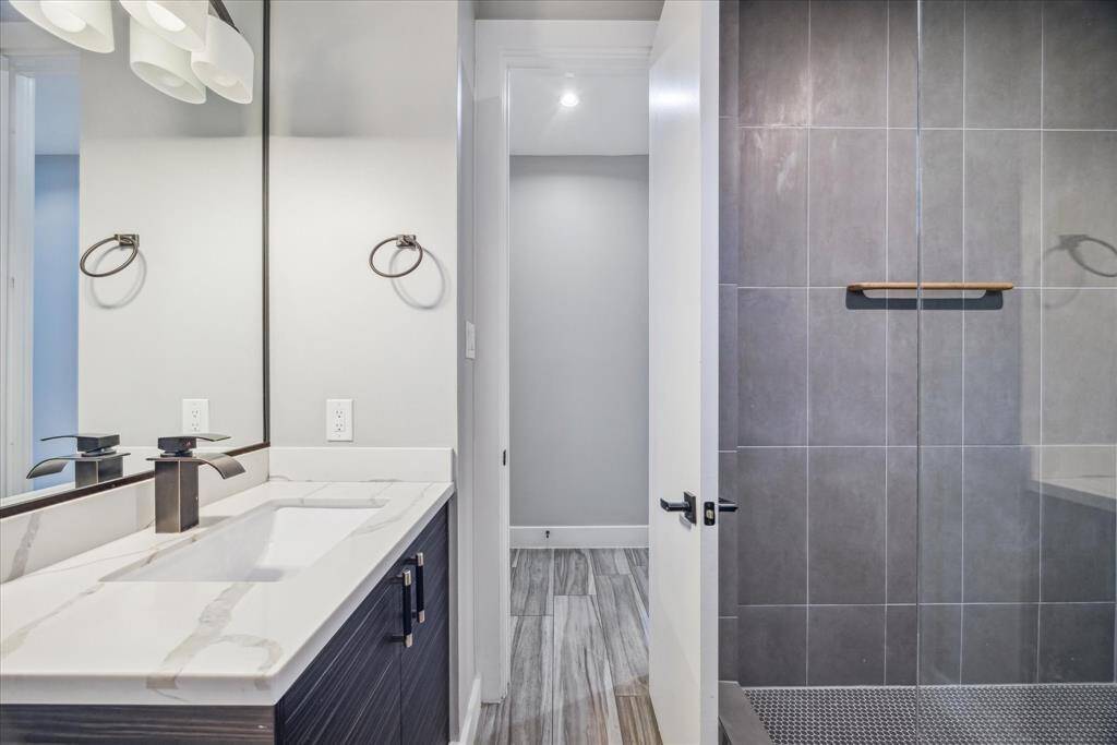 This modern bathroom features a sleek, dual-sink vanity with marble countertops, large mirror, and contemporary fixtures. It includes a spacious, glass-enclosed shower with elegant gray tiling, creating a clean and sophisticated space.