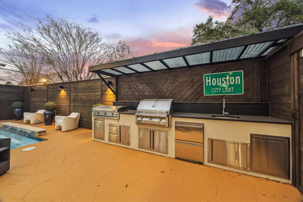 Upgrades galore! This outdoor space features a modern kitchen with a grill and sink, set on a stylish patio, perfect for entertaining or relaxing. The area is enclosed by a wooden fence, providing privacy.