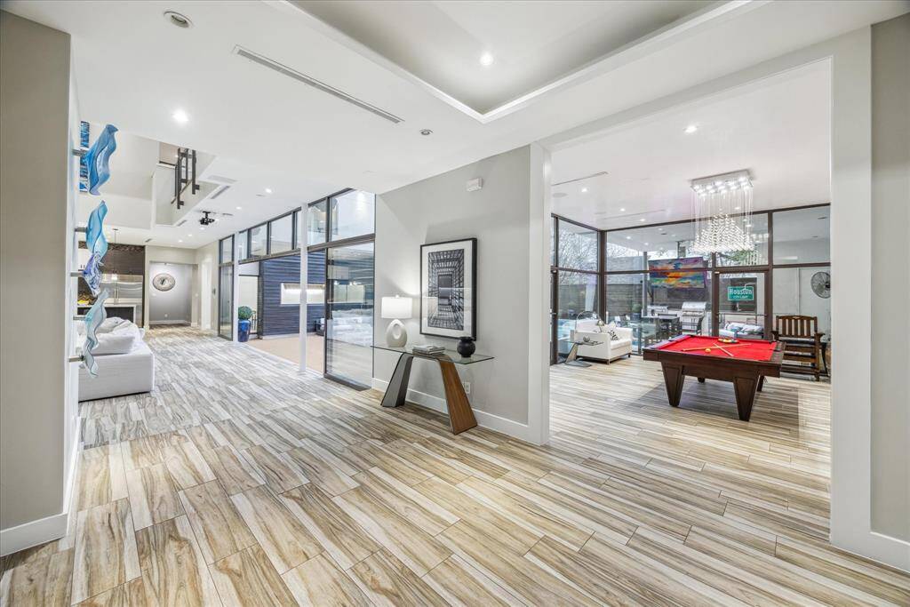 This modern home features a spacious open floor plan with elegant wood-look tile flooring. It boasts large windows for ample natural light and a stylish interior, including a game room with a contemporary lighting fixtures.