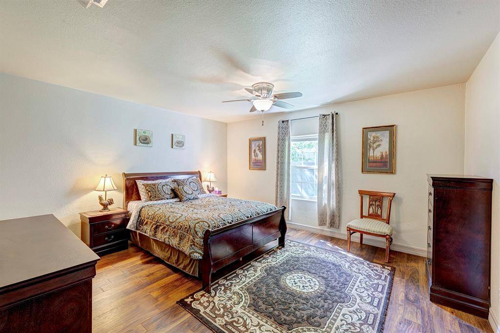 This inviting spacious bedroom features hardwood floors, a ceiling fan, and a window with natural light.