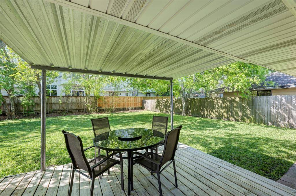 Spacious backyard with a covered patio, featuring a wooden deck. The area is surrounded by a wooden fence and lush greenery, offering a private and inviting outdoor space perfect for relaxation and entertaining.