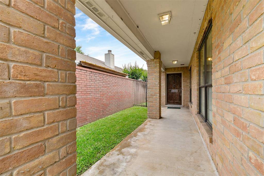 Charming brick-lined front porch with covered walkway, leading to a wooden door. Features outdoor lighting and a small grassy area, offering a welcoming entrance.