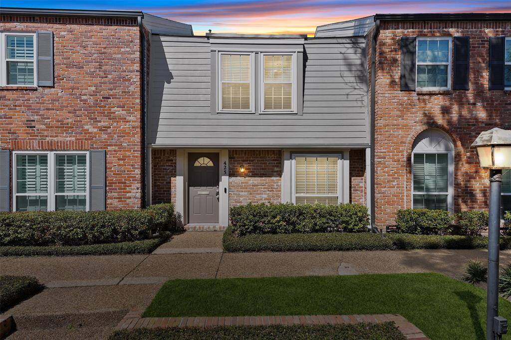 Charming townhouse with classic brick facade and gray siding accents. Features include a welcoming entryway with a modern front door, neatly trimmed hedges, and a well-maintained walkway. Located in a picturesque neighborhood with a cozy, inviting atmosphere.