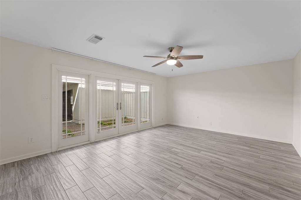 Bright, spacious room with modern gray flooring and a ceiling fan. Features large glass doors leading to an outdoor area, offering plenty of natural light.