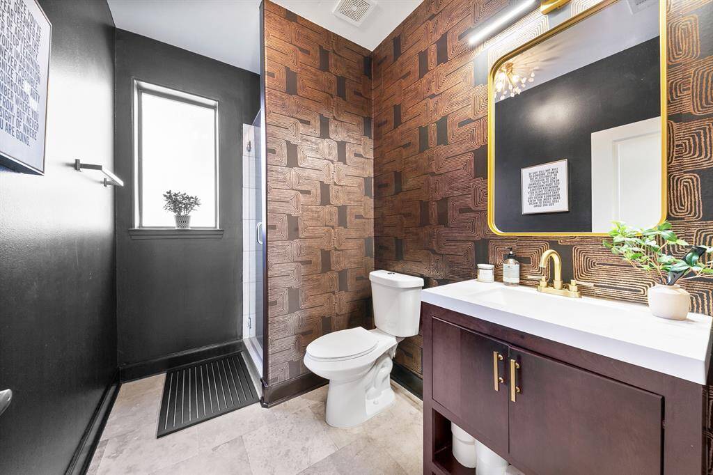 The full guest bath on the first floor boasts magazine-worthy interior design, featuring a sleek tile shower and gorgeous lighting that adds both elegance and practicality to the space. Luxurious fixtures in gold, paired with warm natural tones, elevate the overall aesthetic, creating a rich and inviting atmosphere.