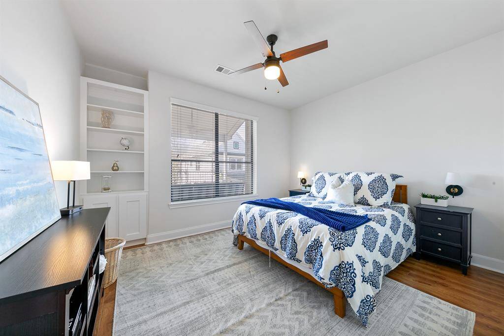 The first of two secondary bedrooms upstairs boasts a spacious walk-in closet, red oak hardwood floors, built-in cabinetry, and a lovely view of the covered patio upstairs and the treetops beyond.