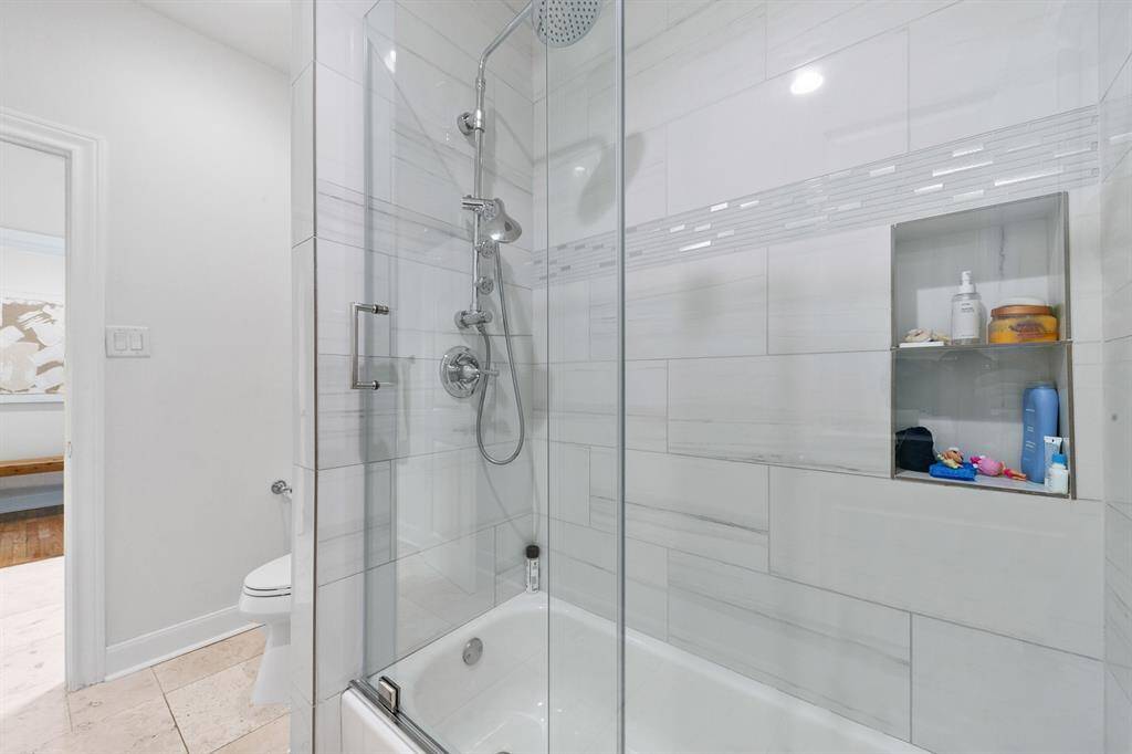 The shared space of the Jack-and-Jill guest bathroom serving the secondary bedrooms features an oversized glass-encased shower/tub combination complete with rain shower head and European wand, floor-to-ceiling tile surround, and built-in shower shelving.