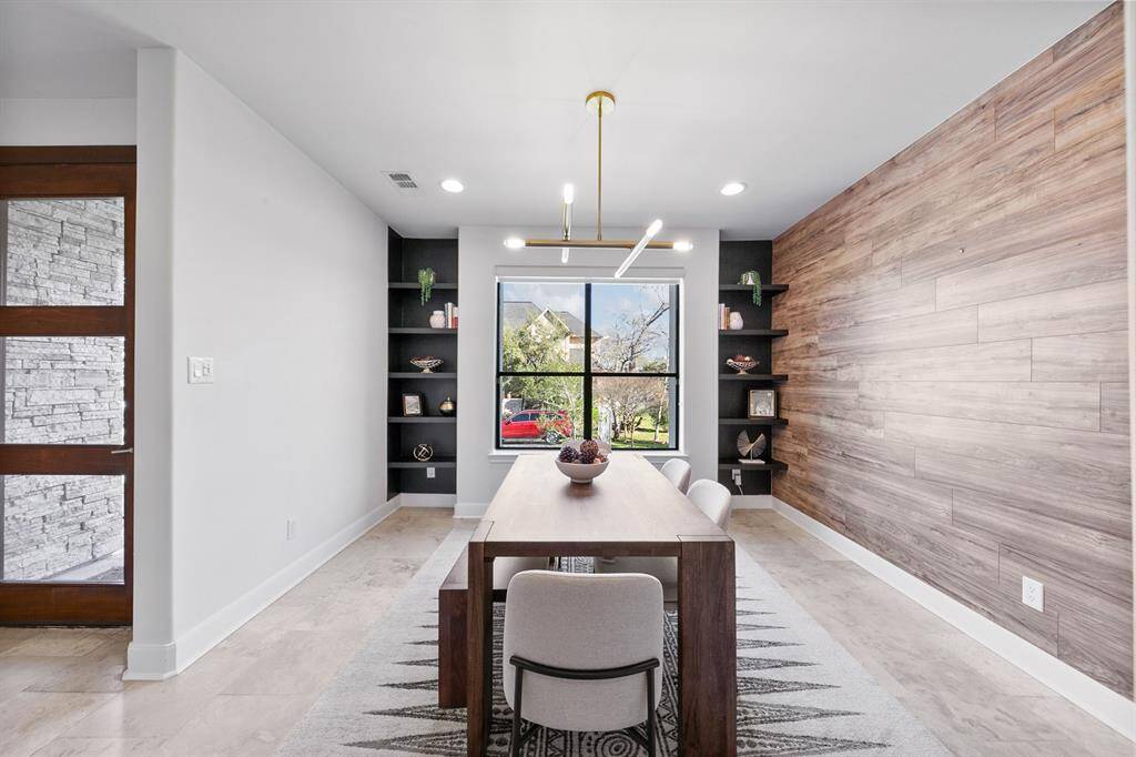 The spacious dining area is thoughtfully designed with symmetry. Centered between built-ins of floating shelves, the large picture window anchors the room, flooding it in natural light by day.