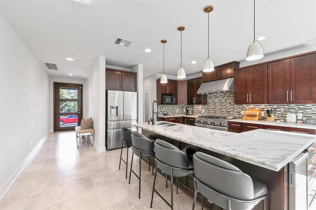 The spacious island kitchen features marble countertops and a full mosaic tile backsplash and is equipped with Kitchen-Aid appliances, most notably a gas range with double ovens. The countertop seating provides the ultimate in entertaining flexibility, perfect for casual gatherings, homework during meal prep, breakfasts, and after-school snacks.  An under-counter drink cooler is located just to the right of the bar stools, refreshing family and friends without the need to intrude into the kitchen itself.
