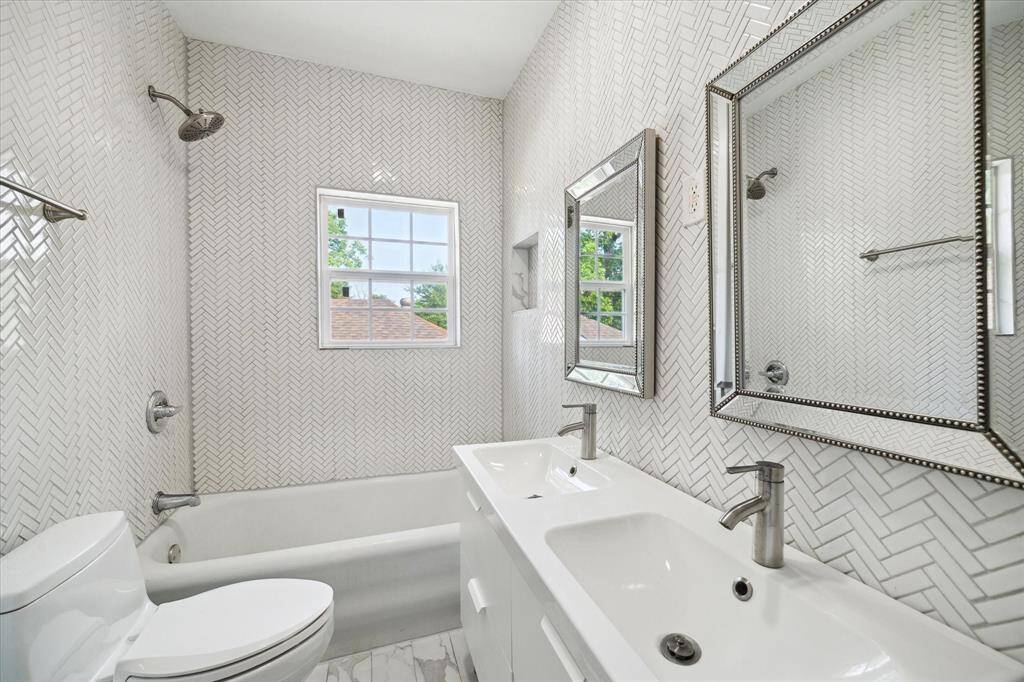 Shared renovated hall bath with dual sinks, framed mirrors, herringbone accent feature wall, and full tub/shower