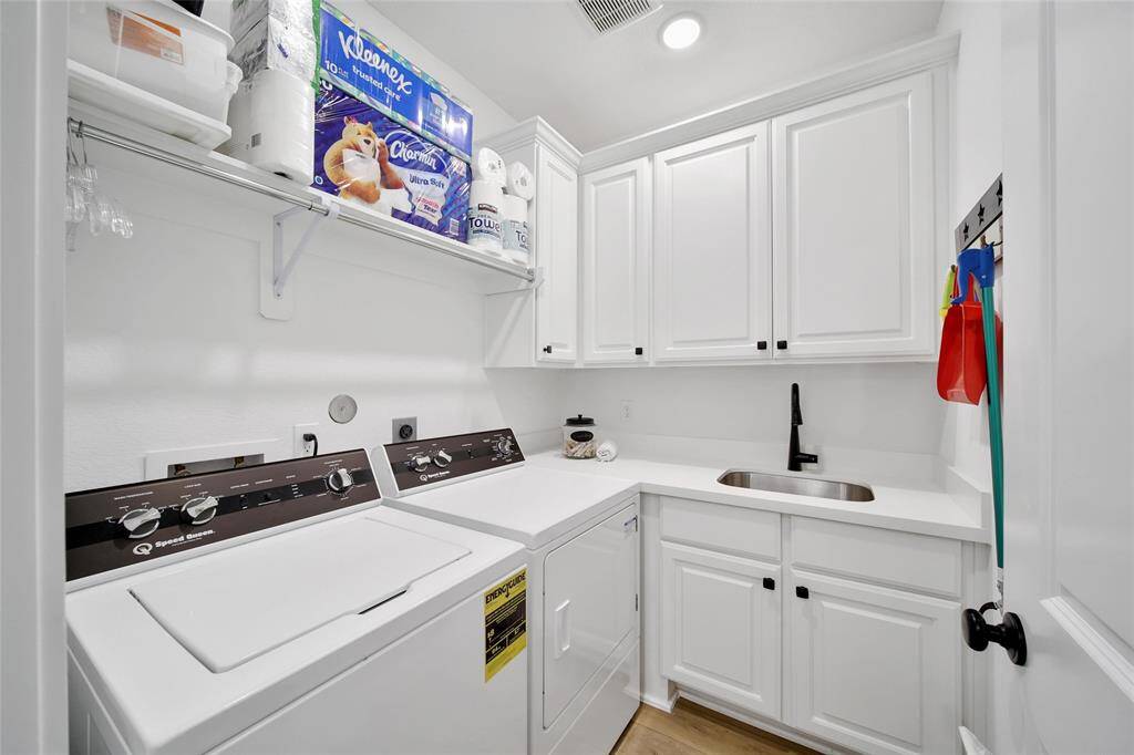 The handy utility room offers built-in cabinets, spacious countertops for folding, and a convenient sink for washing and cleaning chores, while also providing ample storage for supplies.