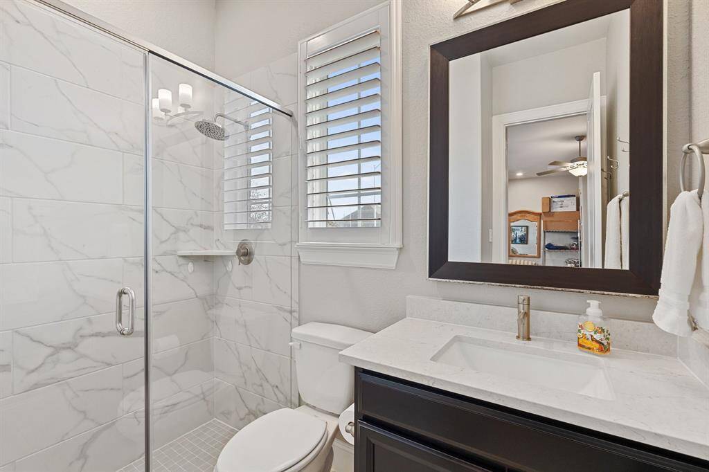 This stylish bathroom features a spacious tiled walk-in shower, a sleek vanity with a sink, and a toilet, creating a modern and functional space.