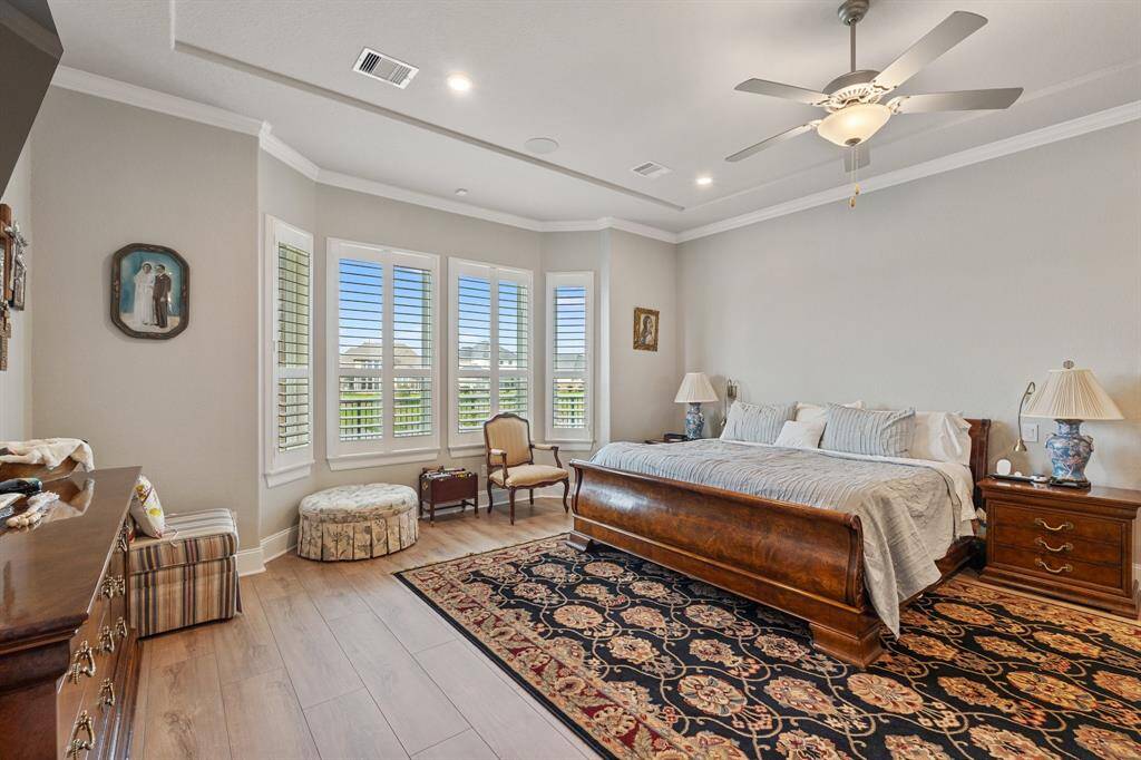 The spacious primary bedroom boasts elegant crown molding, multiple windows with privacy blinds, and beautiful engineered wood flooring, offering a serene and stylish retreat.