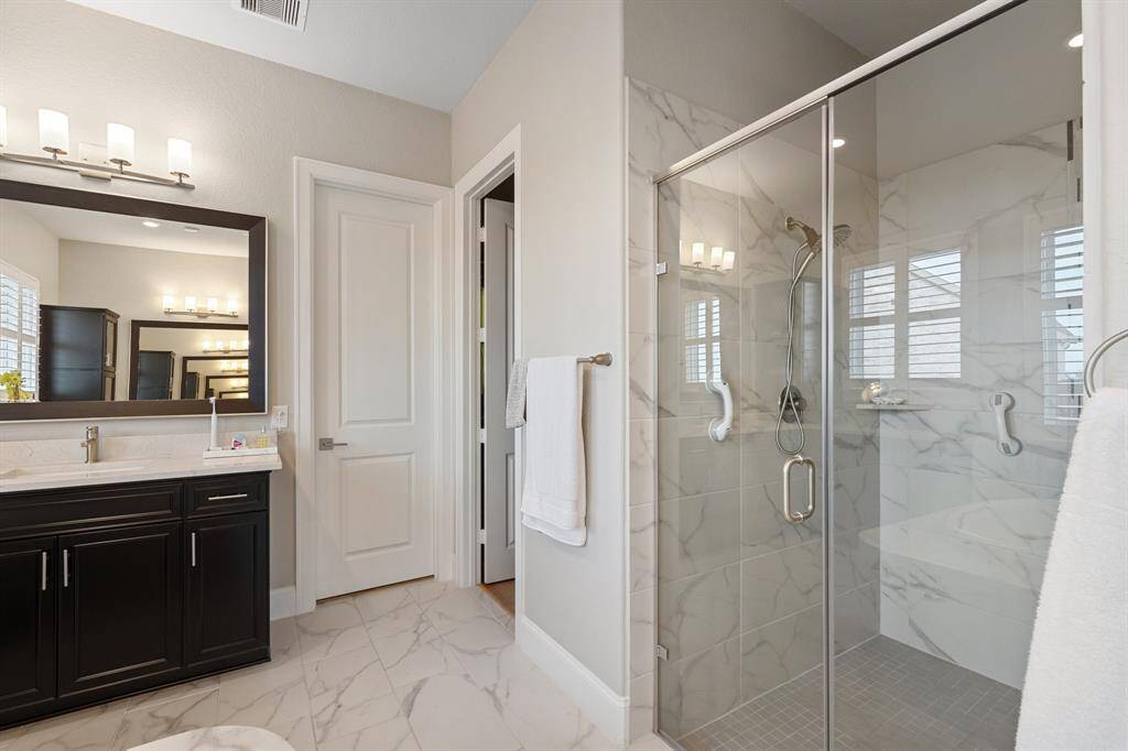 The primary bathroom also boasts a spacious, tiled walk-in shower, elegant tile flooring, and custom paint, adding a touch of luxury and style to the room.