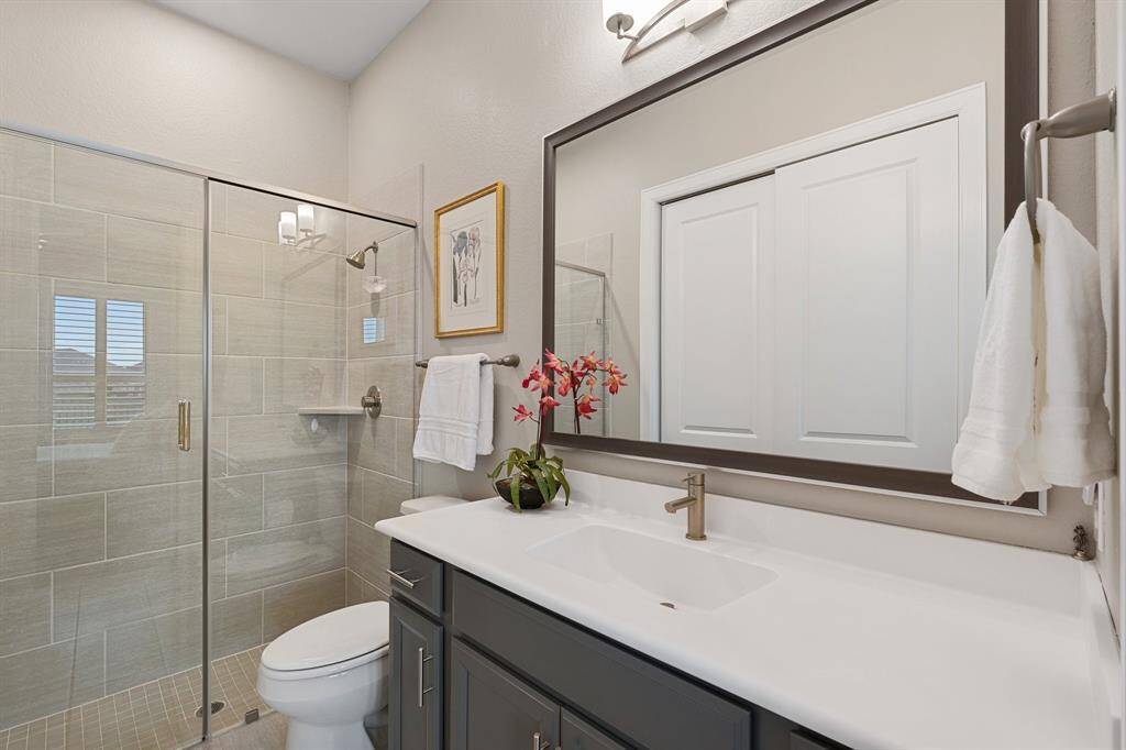 This elegant bathroom boasts a large tiled walk-in shower, a sleek toilet, and an oversized sink vanity, offering both style and functionality.