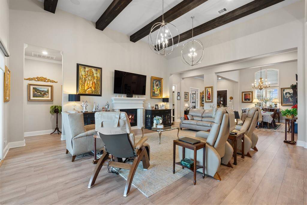 The expansive living room is a true showstopper, featuring custom paint, soaring high ceilings with elegant wood beams, a cozy fireplace, engineered wood flooring, and multiple windows with privacy shades that fill the space with natural light!