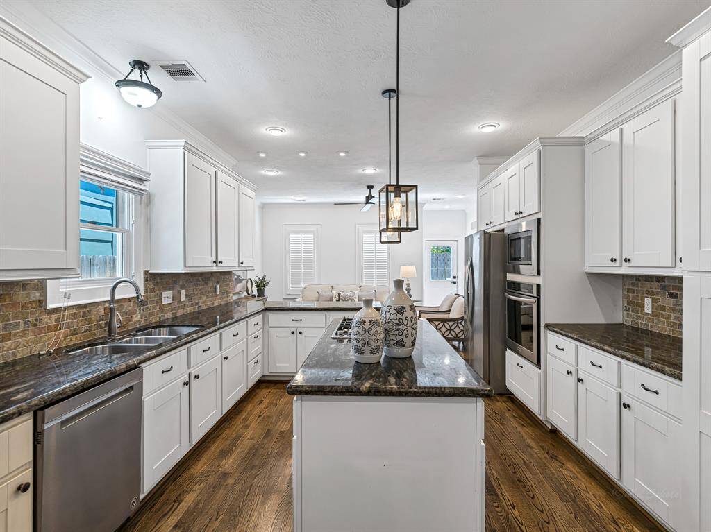 The kitchen is a chef’s dream, showcasing stainless steel appliances, sleek granite countertops, a tumbled stone subway tile backsplash, shaker-style cabinets, and pendant lighting with Edison bulbs for a stylish touch.
