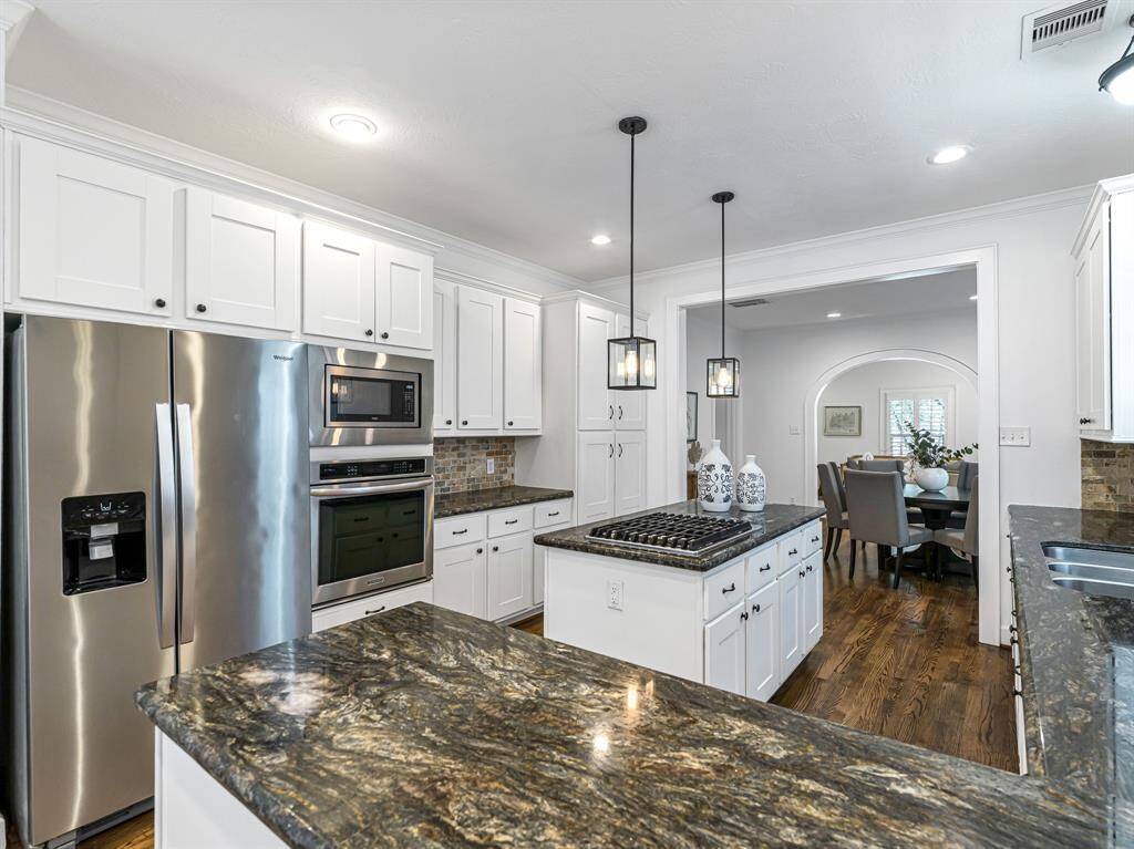 Perfect for entertaining, this kitchen effortlessly connects the dining room and cozy den. The refrigerator, microwave, and oven are seamlessly integrated into the wall with custom cabinetry. The island features a gas cooktop and offers ample storage on both sides.