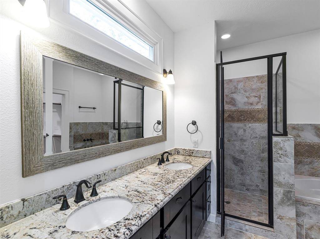The luxurious primary bathroom features dual sinks, sleek espresso cabinetry, complementary granite, and oil-rubbed bronze finishes. Above, a large framed mirror is complemented by a lengthy transom window, adding natural light and a touch of elegance.
