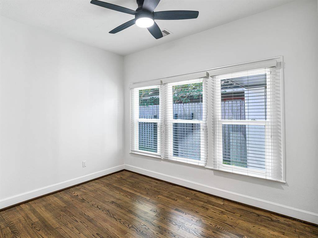 This charming secondary bedroom offers a spacious closet, wood floors, a ceiling fan, and bright windows. Additional storage is conveniently accessed through a small door.