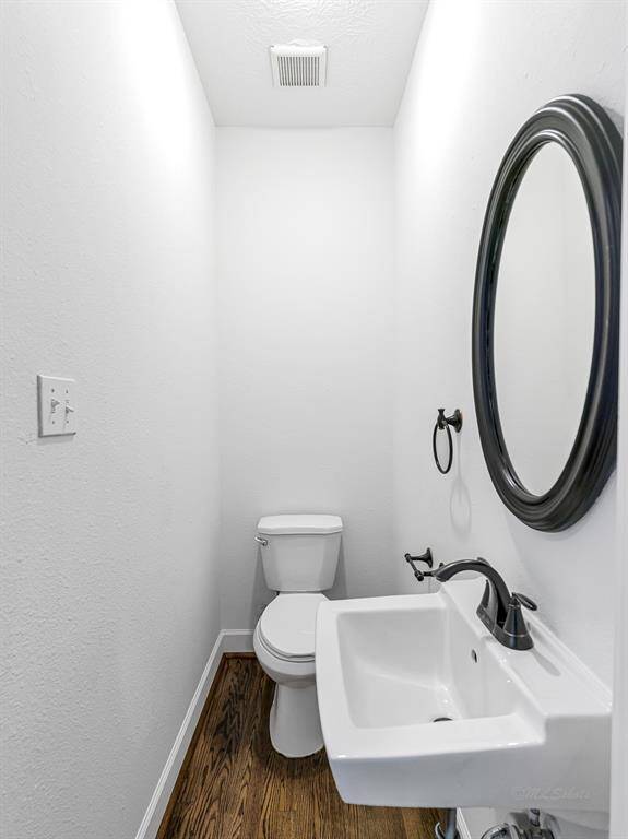 A convenient half bath features wood floors, a pedestal sink, and an oval-framed mirror.