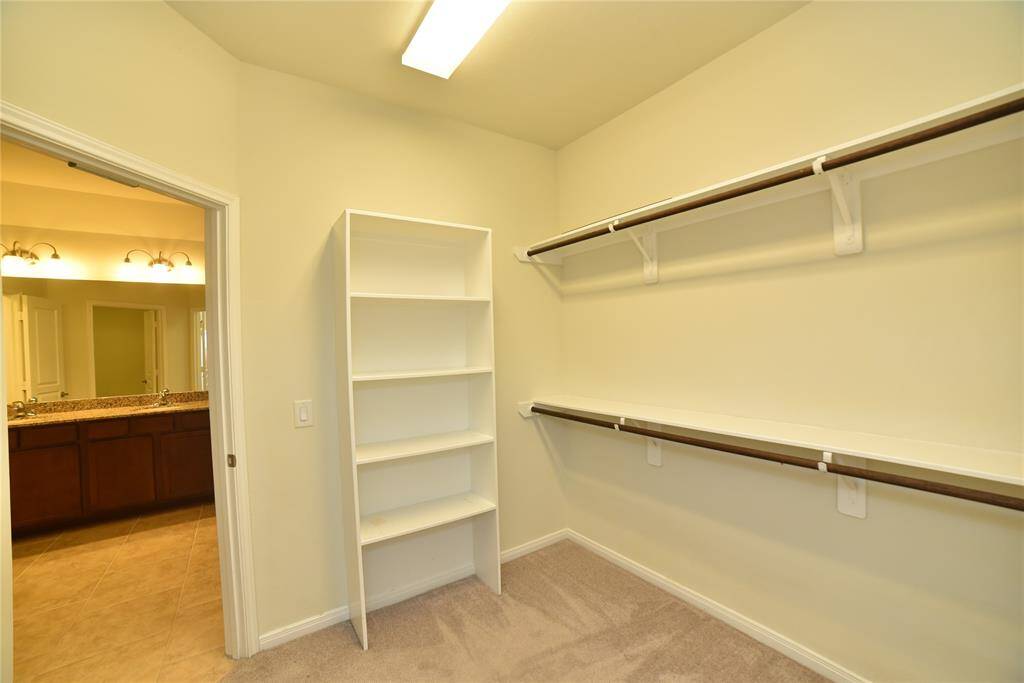 This photo shows a spacious walk-in closet with built-in shelving and hanging rods, featuring neutral walls and carpet. It connects to a bathroom with granite countertops and ample lighting.