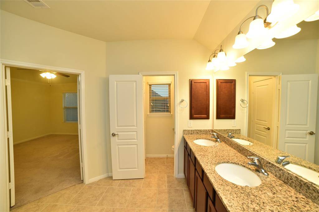 This photo shows a bright bathroom featuring a double vanity with granite countertops, modern fixtures, and ample lighting. It connects to a bedroom through an open doorway, offering convenience and accessibility.